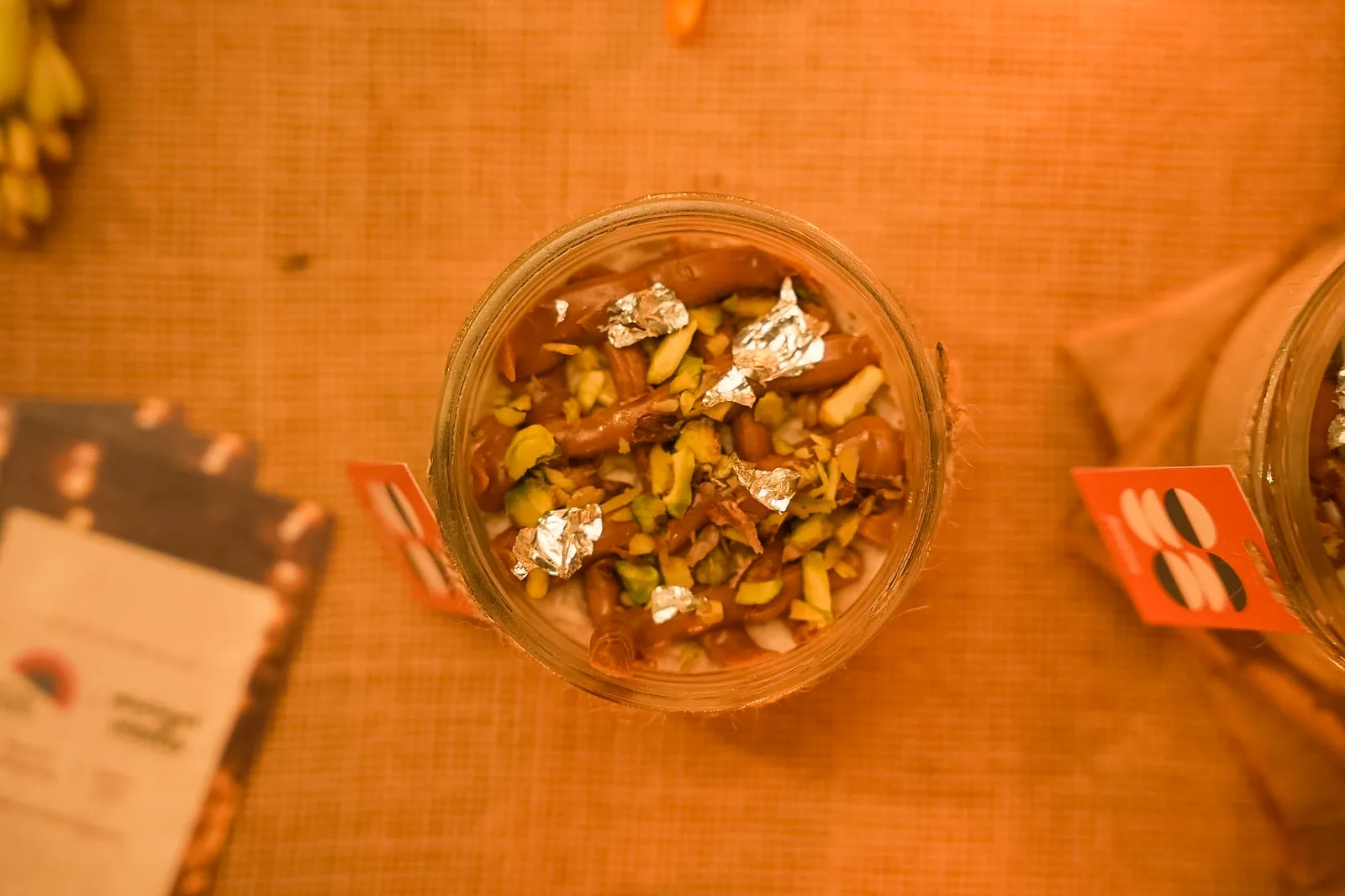 A jar of Biscoff kalakand from above, with pistachios and silver leaf