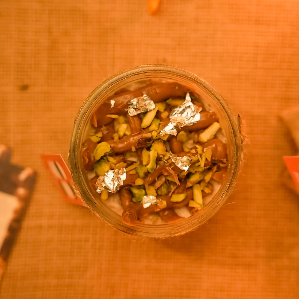 A jar of Break of Dawn Biscoff kalakand from above, with pistachios and silver leaf