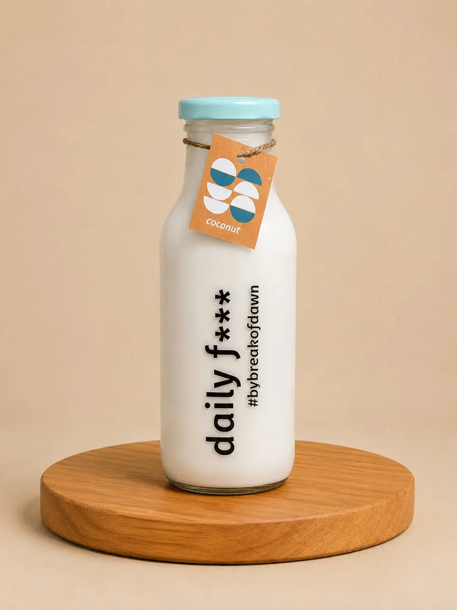 A bottle of Break of Dawn fresh coconut milk on a wooden board against a soft tan backdrop.