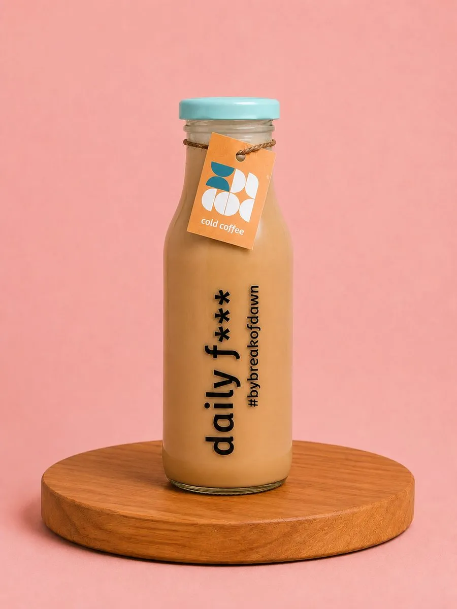 A bottle of Break of Dawn cold coffee on a wooden board against a soft pink backdrop.