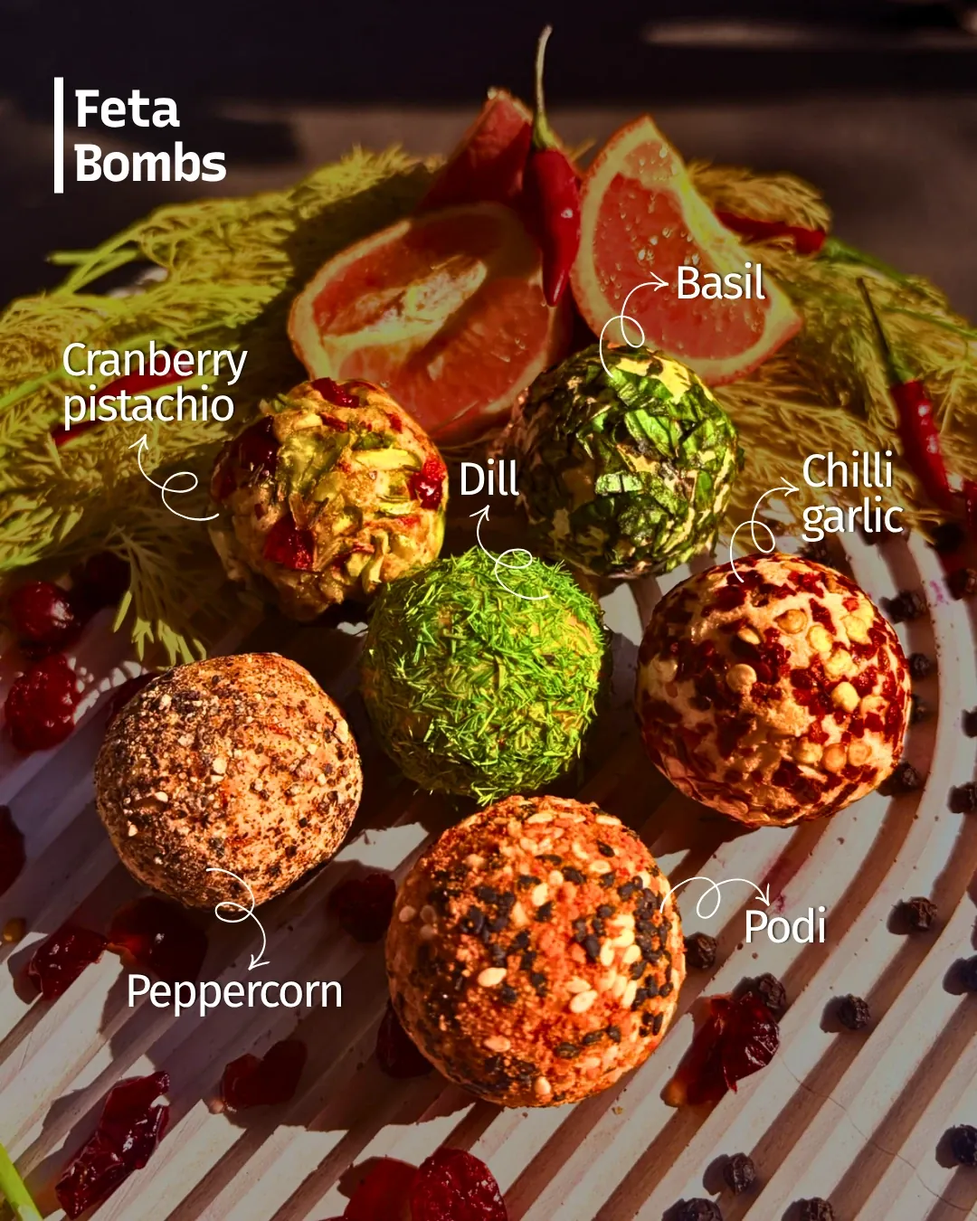 Six feta bombs on a striped wooden board with blood orange, fennel, red chillies and cranberries, each flavour labelled