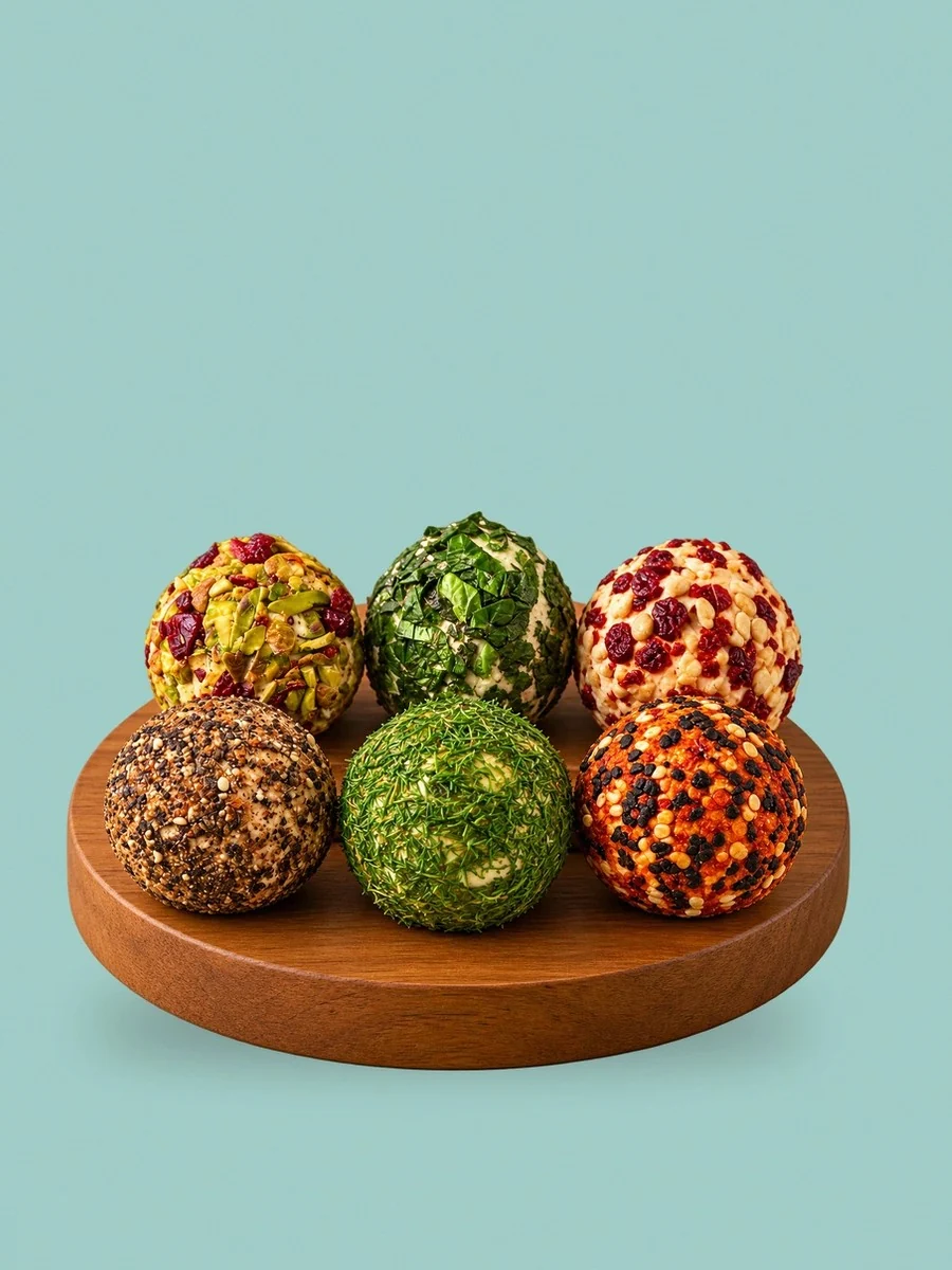 A walnut board of six Break of Dawn feta bombs: cranberry pistachio, basil, chilli garlic, peppercorn, dill and podi